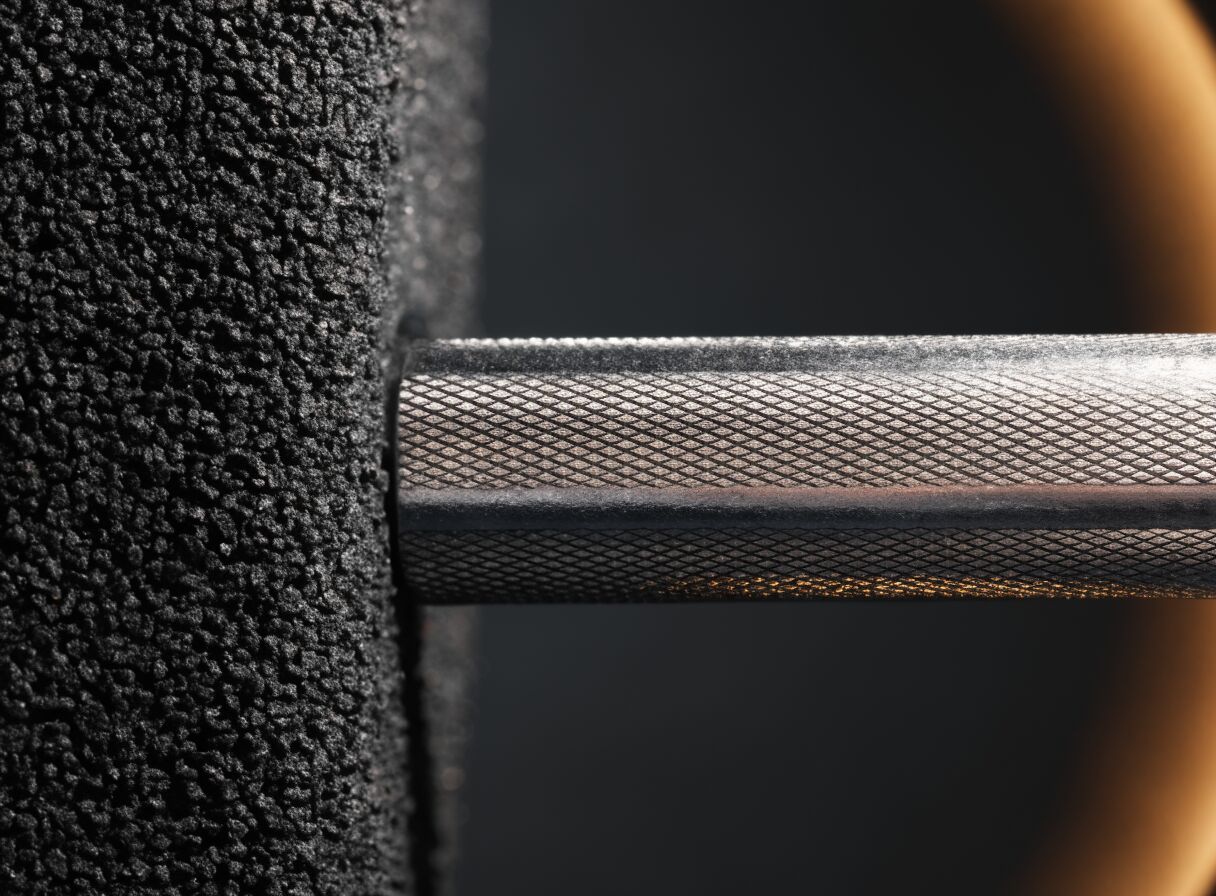 Macro photograph of black rubber gym tile texture beside a knurled steel barbell shaft